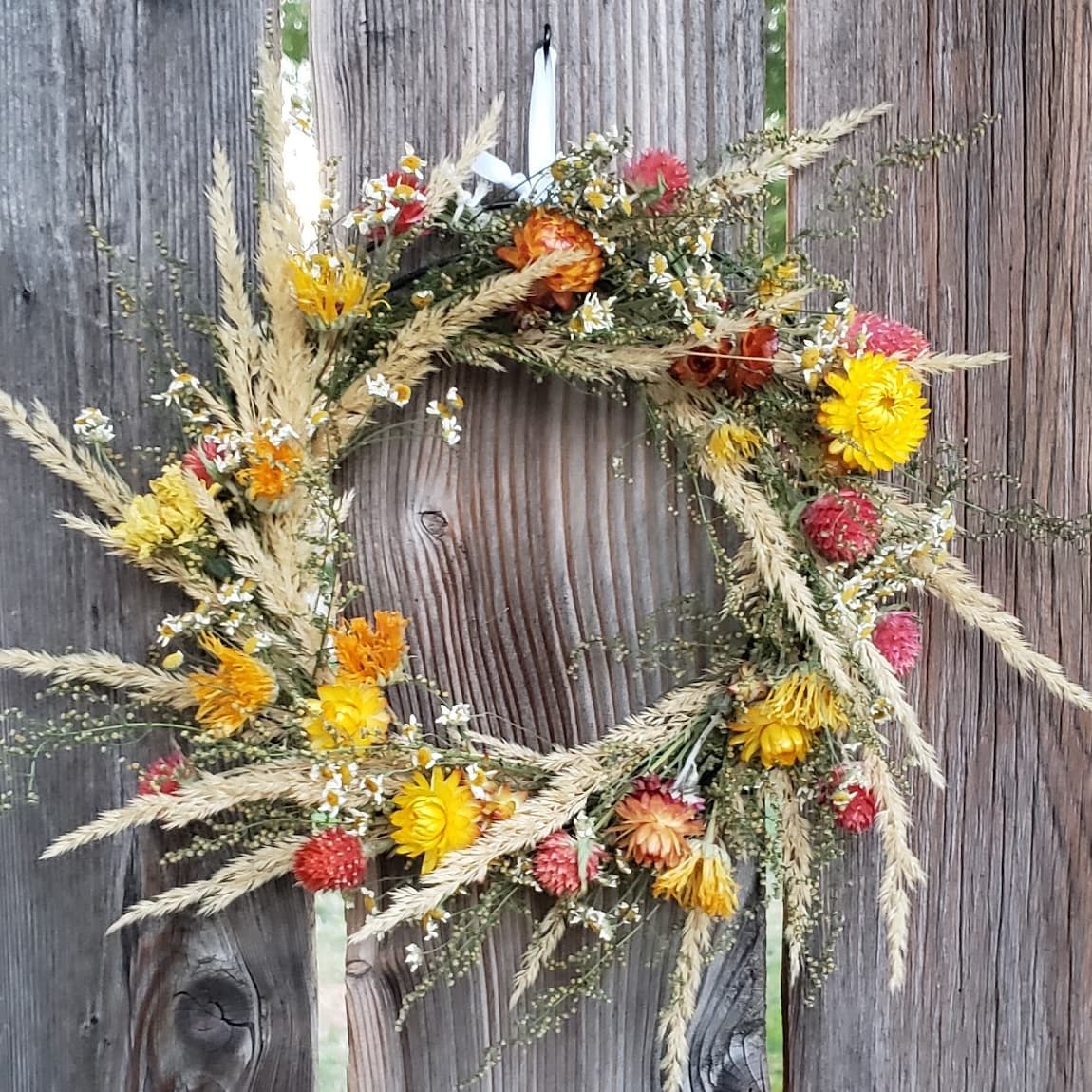 A dried flower wreath hanging on a weathered fence